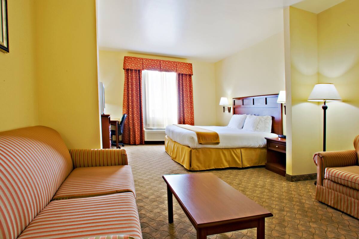 A hotel room with a bed, a sofa, a table, and a desk with a lamp.