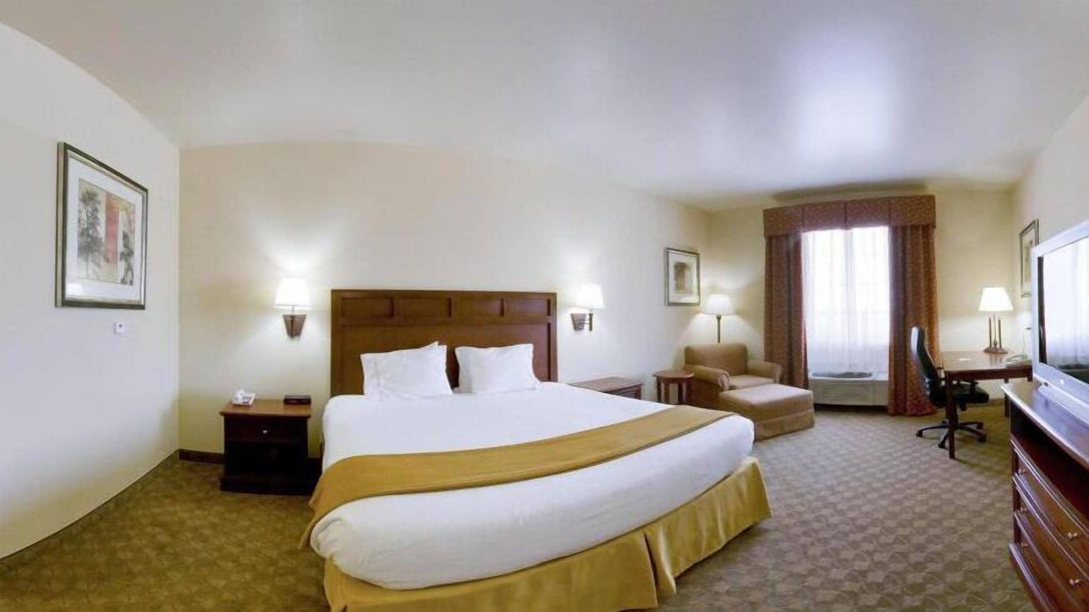 A hotel room with a large bed, a desk, a chair, a television, and two lamps.