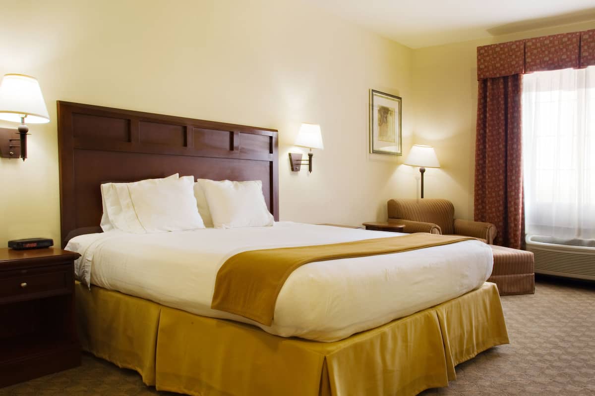 A hotel room with a large bed, two bedside tables, a chair, a window with curtains, and a wall-mounted picture.