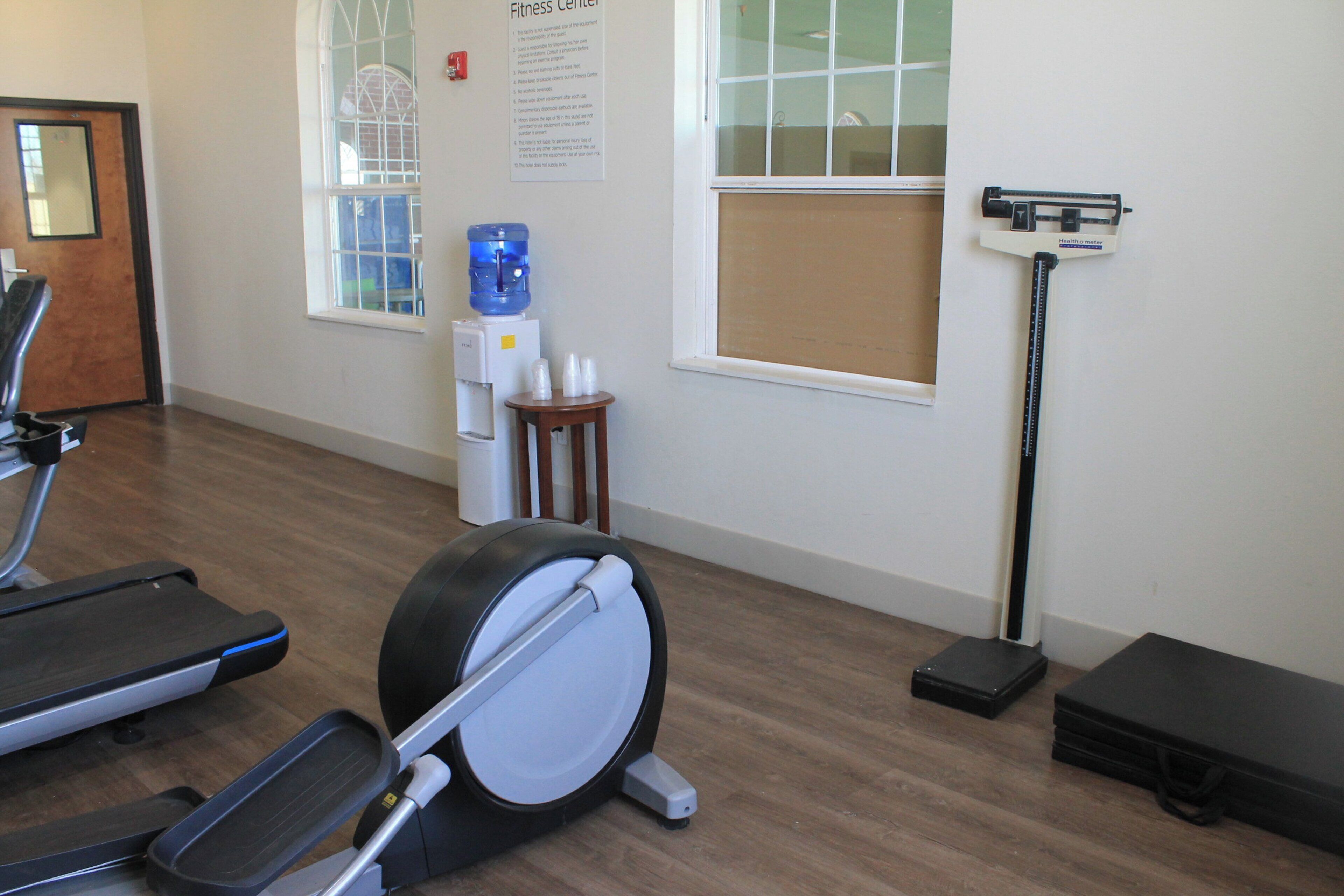 A fitness center with exercise equipment, a water cooler, and a window with blinds.