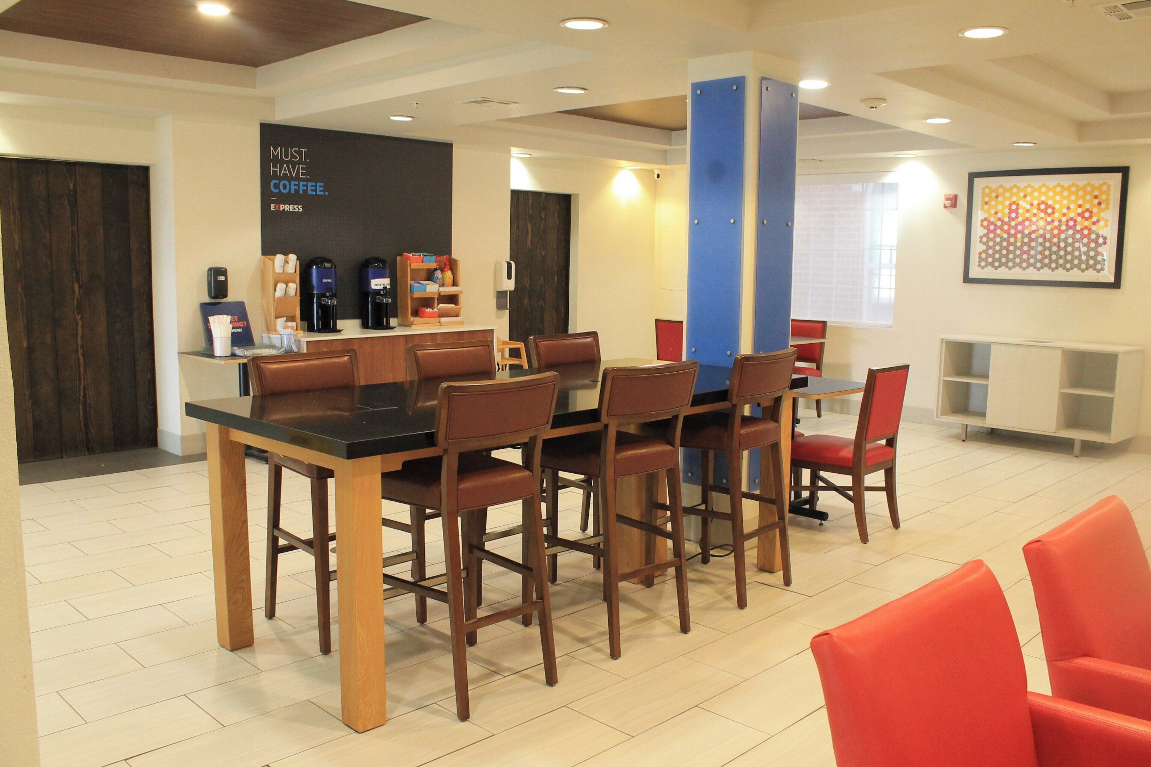 A modern dining area with a black table and brown chairs, a coffee station, and a framed artwork on the wall.