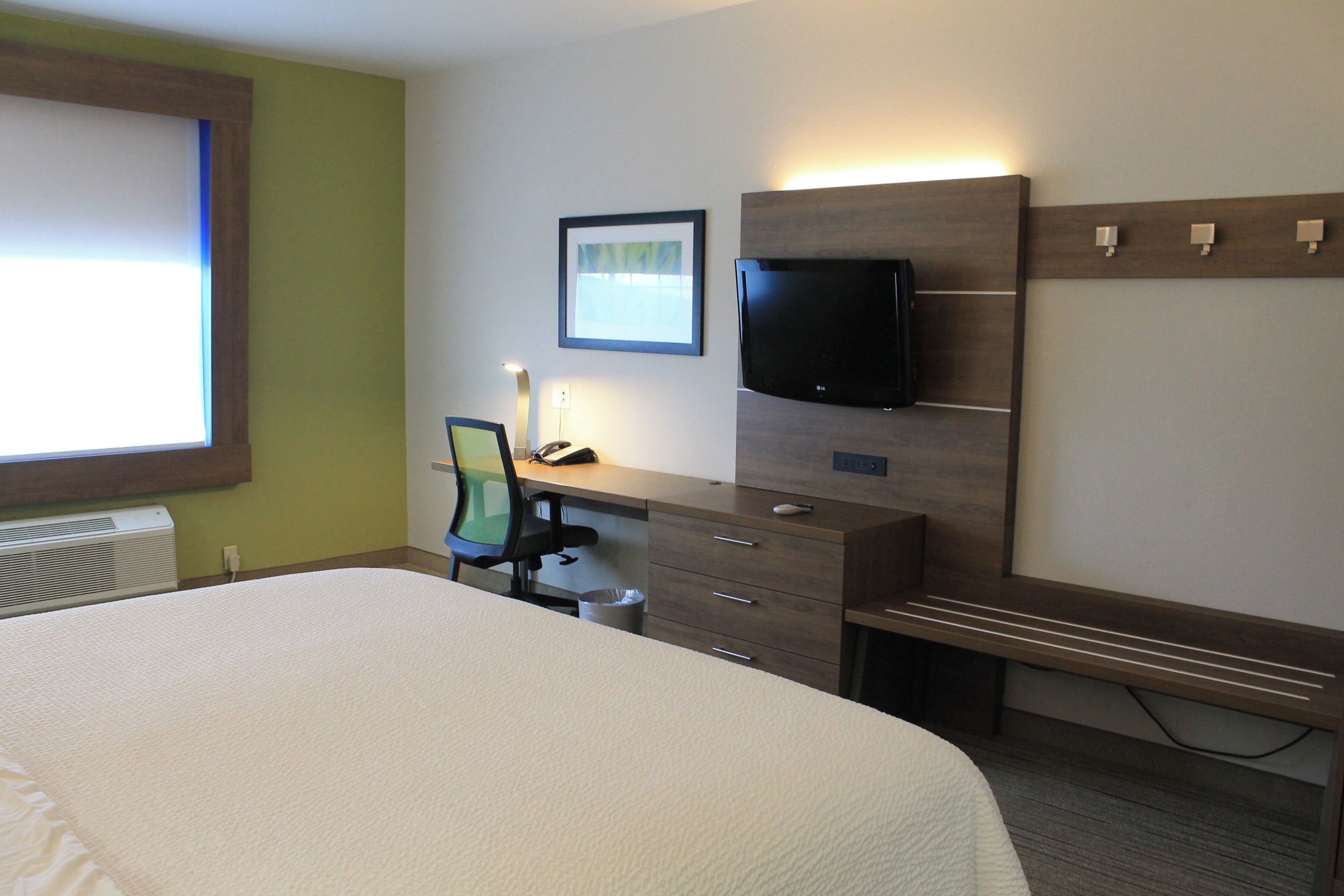 Una habitación de hotel con cama, escritorio, silla, televisor y ventana.