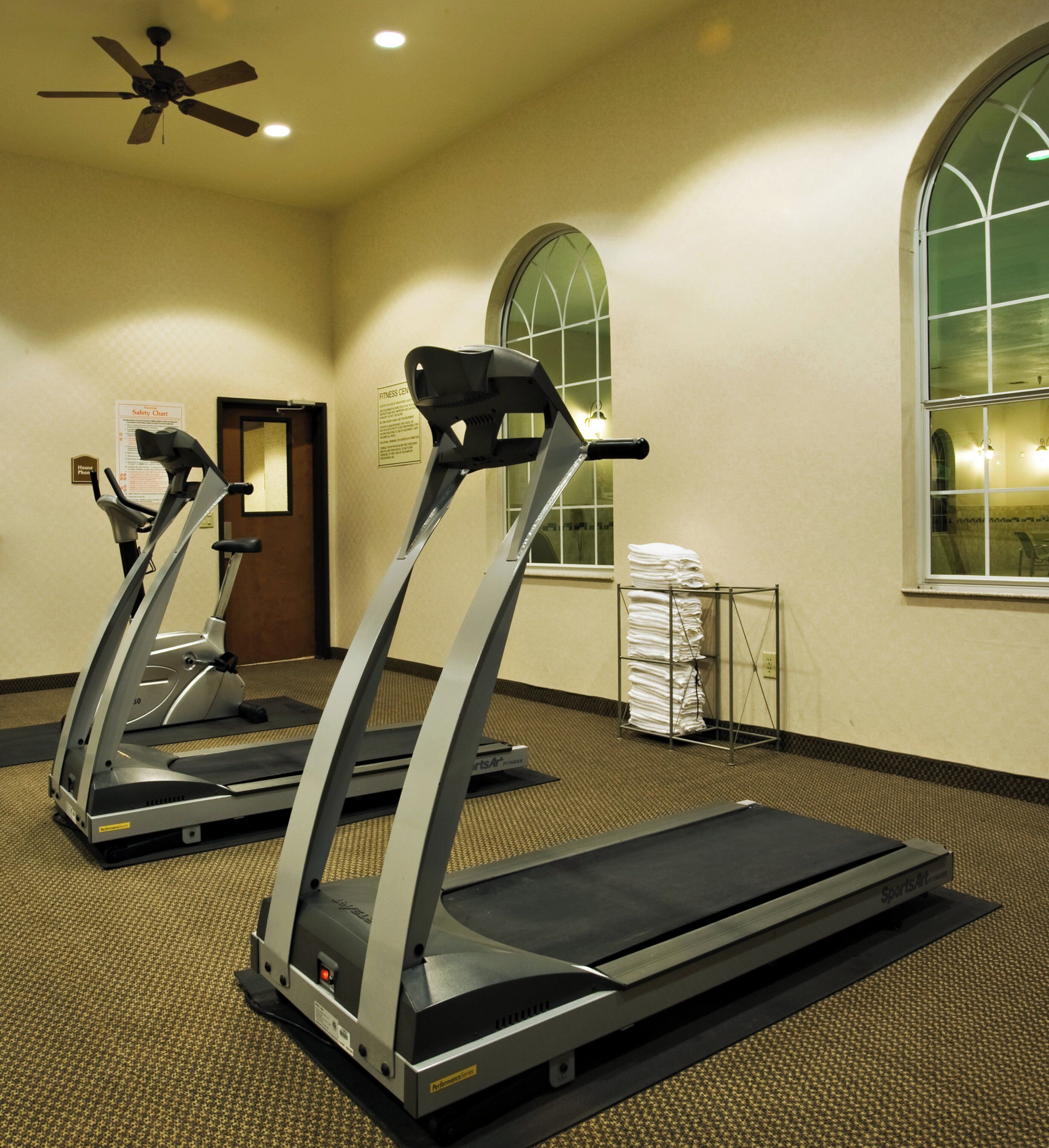 A fitness center with treadmills, a fan, and a safety chart on the wall.
