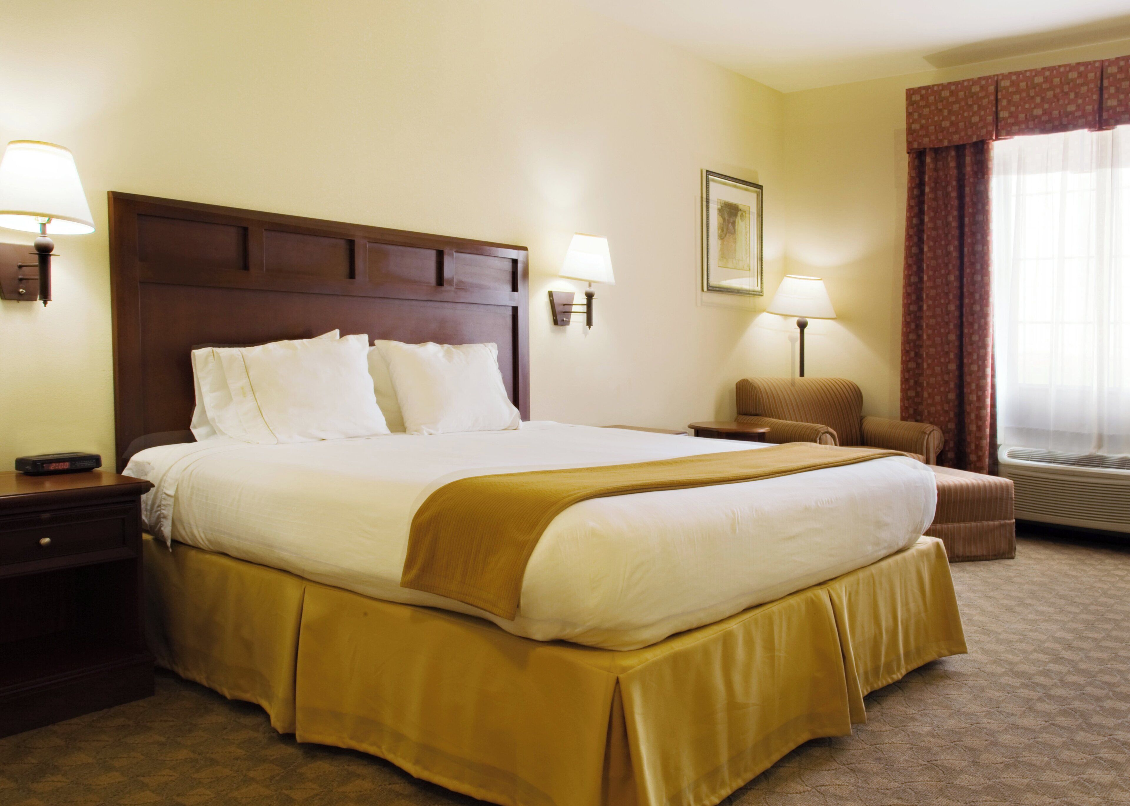 A hotel room with a large bed, bedside lamps, a chair, a nightstand, and a window with curtains.