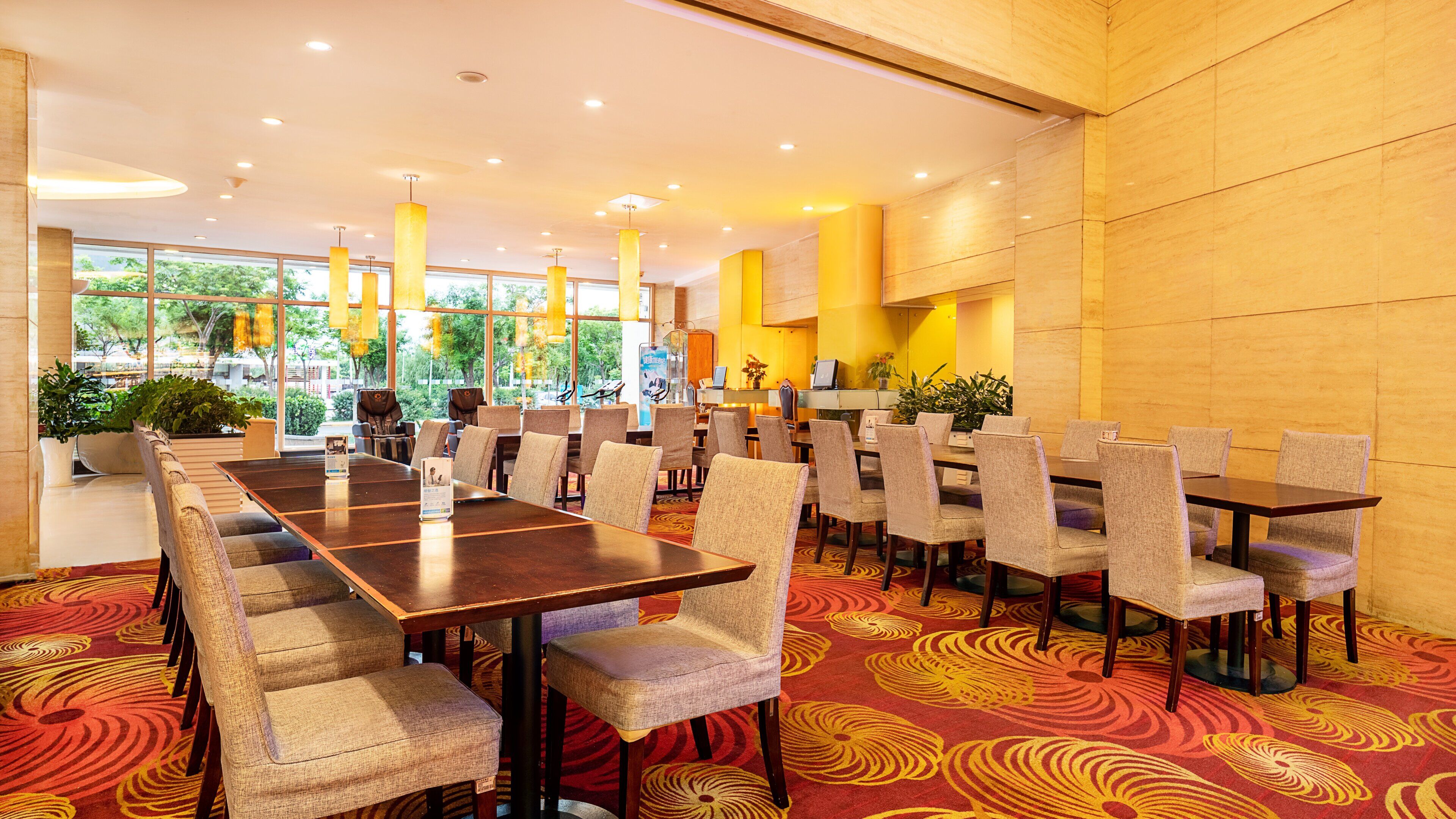 A conference room with multiple tables and chairs, large windows with natural light, and a carpeted floor.