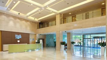 A spacious lobby with a reception desk, a glass elevator, and a second-floor balcony.