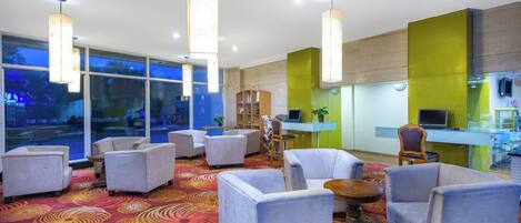A hotel lobby with seating, a reception desk, and large windows.