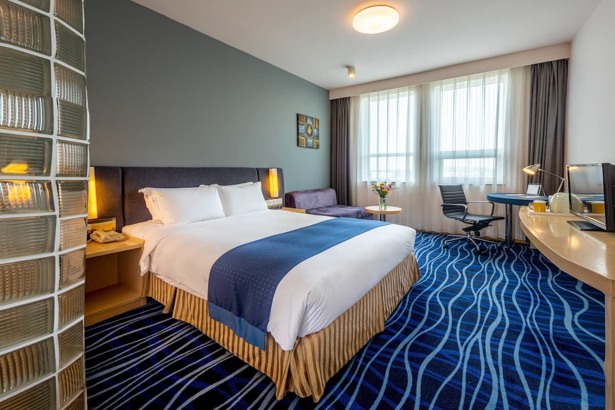 A hotel room with a large bed, a desk, a chair, a TV, and a window with curtains.