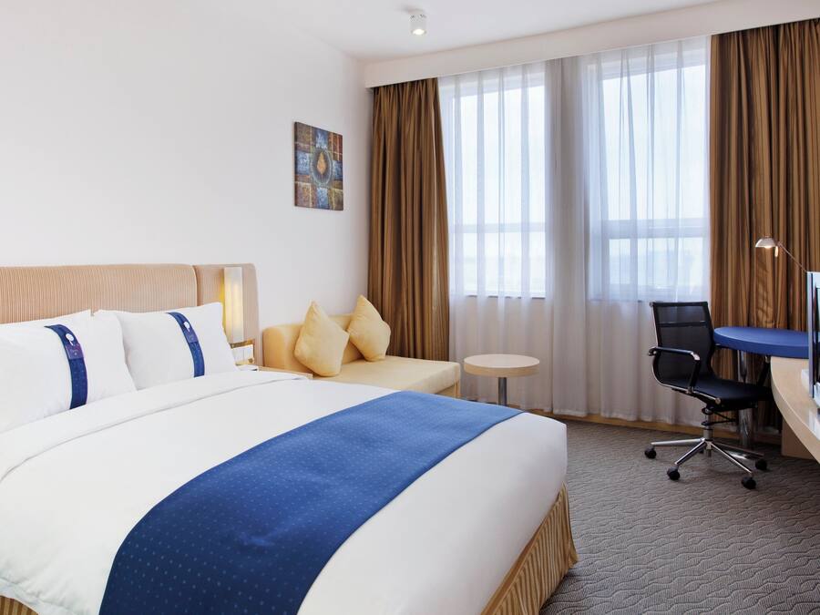 A hotel room with a large bed, a desk, a chair, and a television.