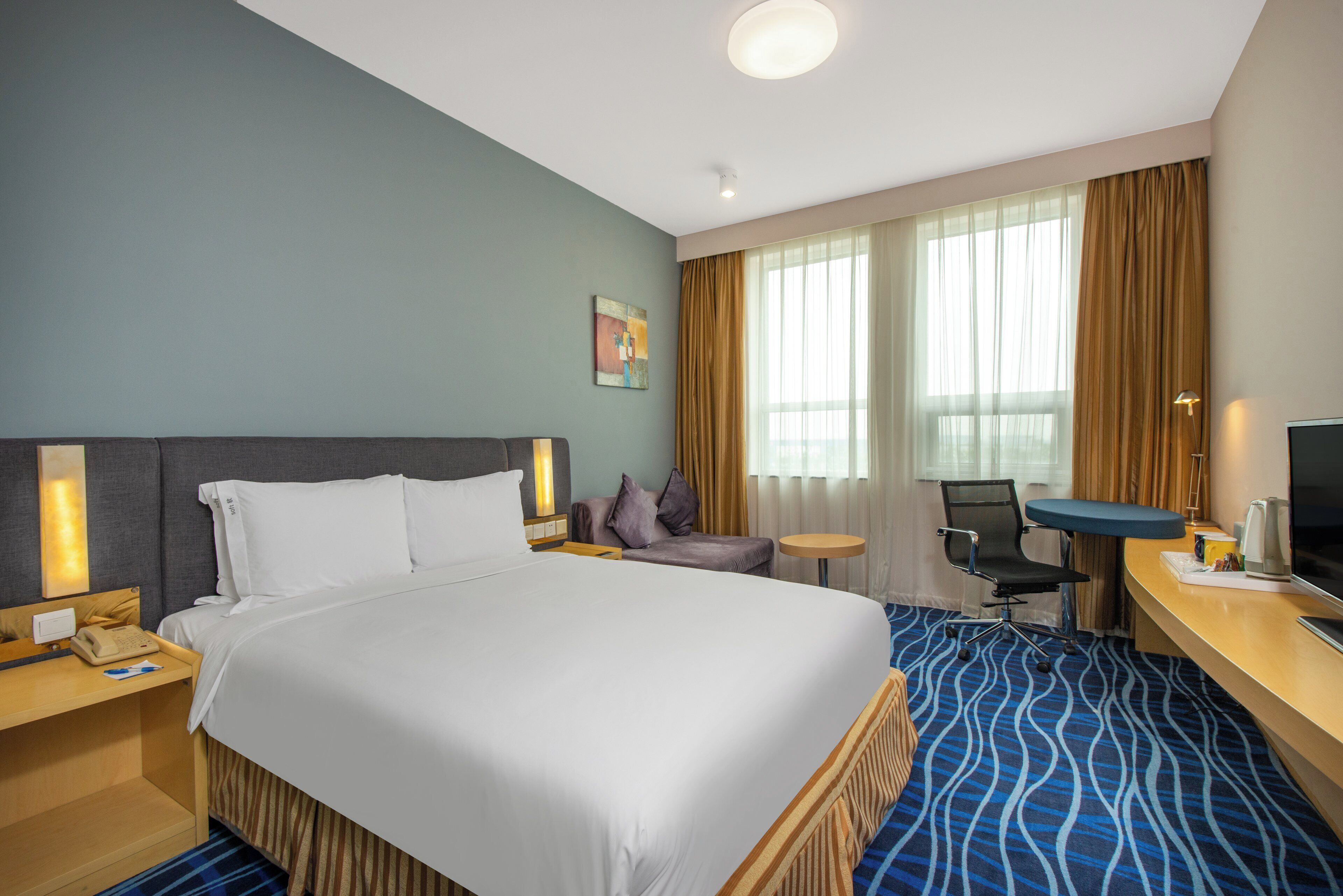 A hotel room with a large bed, a desk with a chair, a television, and a window with curtains.