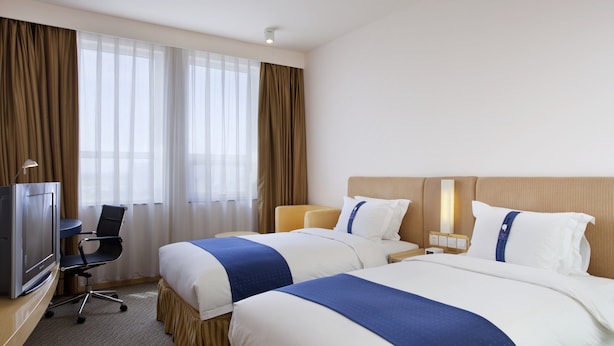 A hotel room with two beds, a desk with a computer, a TV, and a large window with curtains. - Holiday Inn Express Airport Tianjin by IHG (Tianjin)