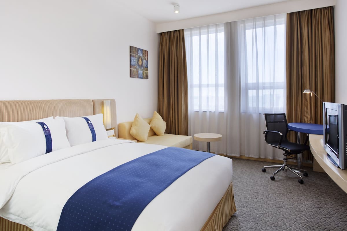 A hotel room with a large bed, a desk, a chair, and a television.