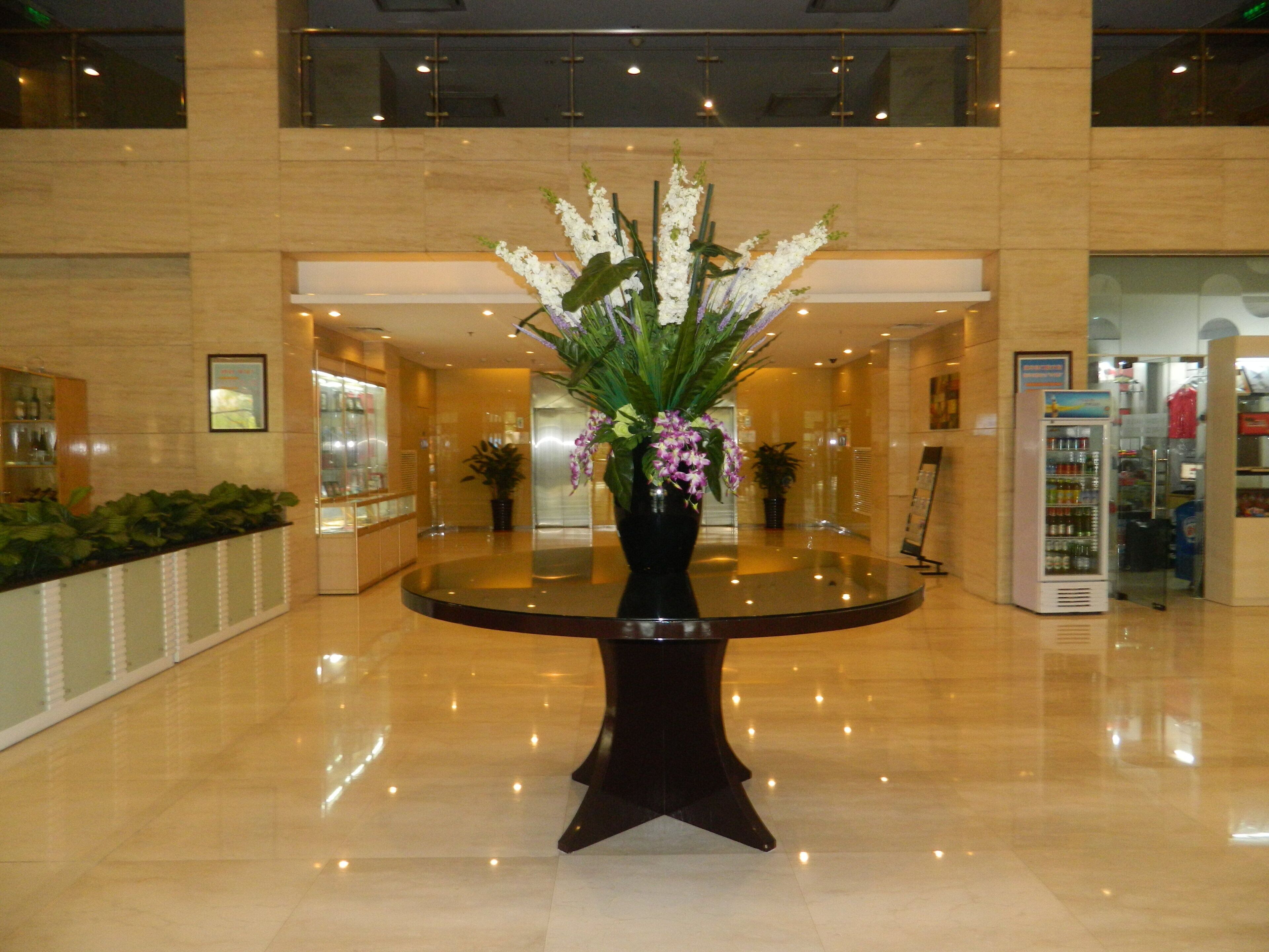 A lobby with a round table, a potted plant, and a vending machine.