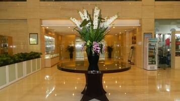 A lobby with a round table, a potted plant, and a vending machine.