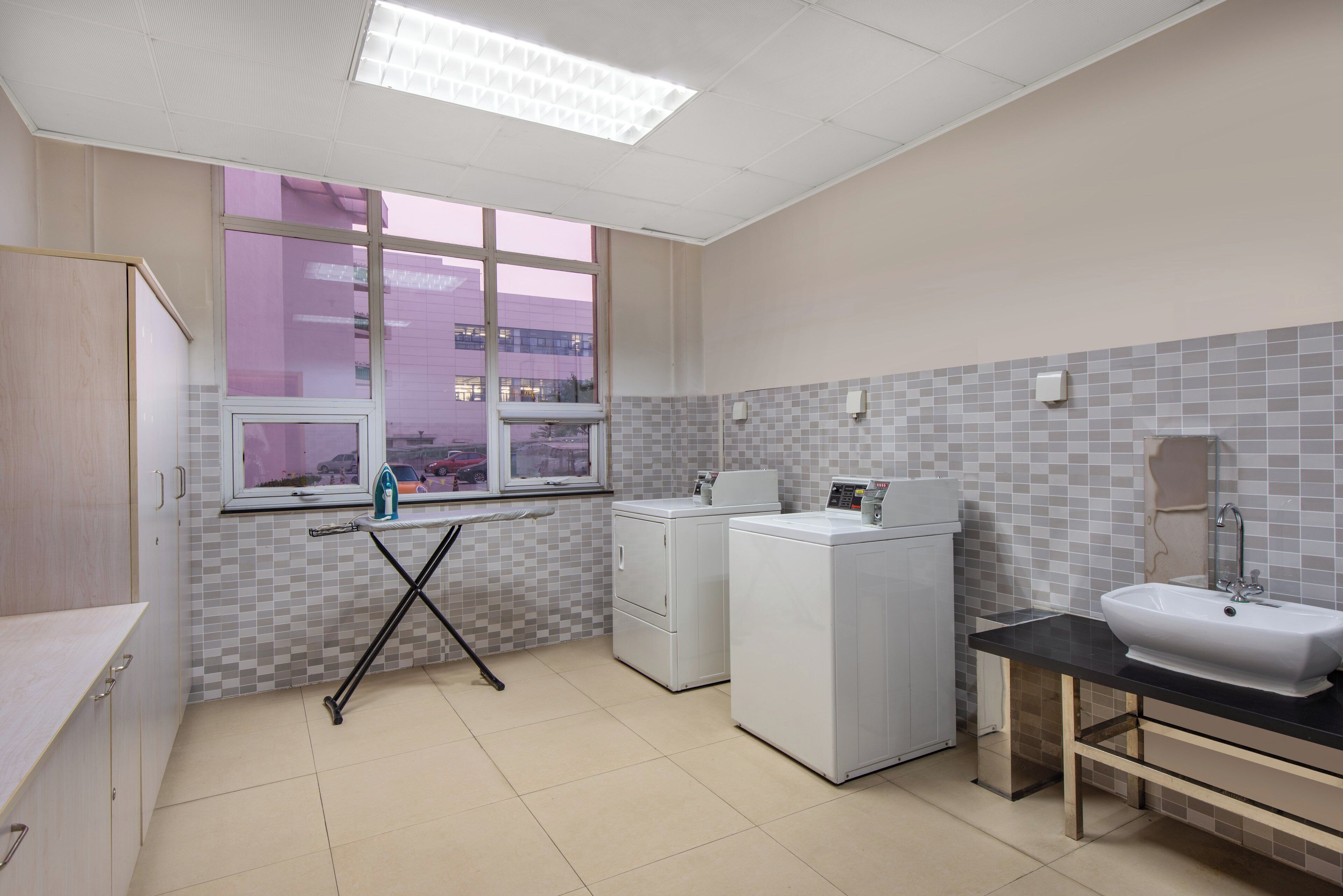 A laundry room with a window, washing machines, a sink, and a tiled backsplash.