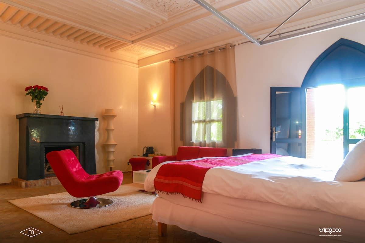 A bedroom with a bed, a red chair, a fireplace, and a window with curtains.