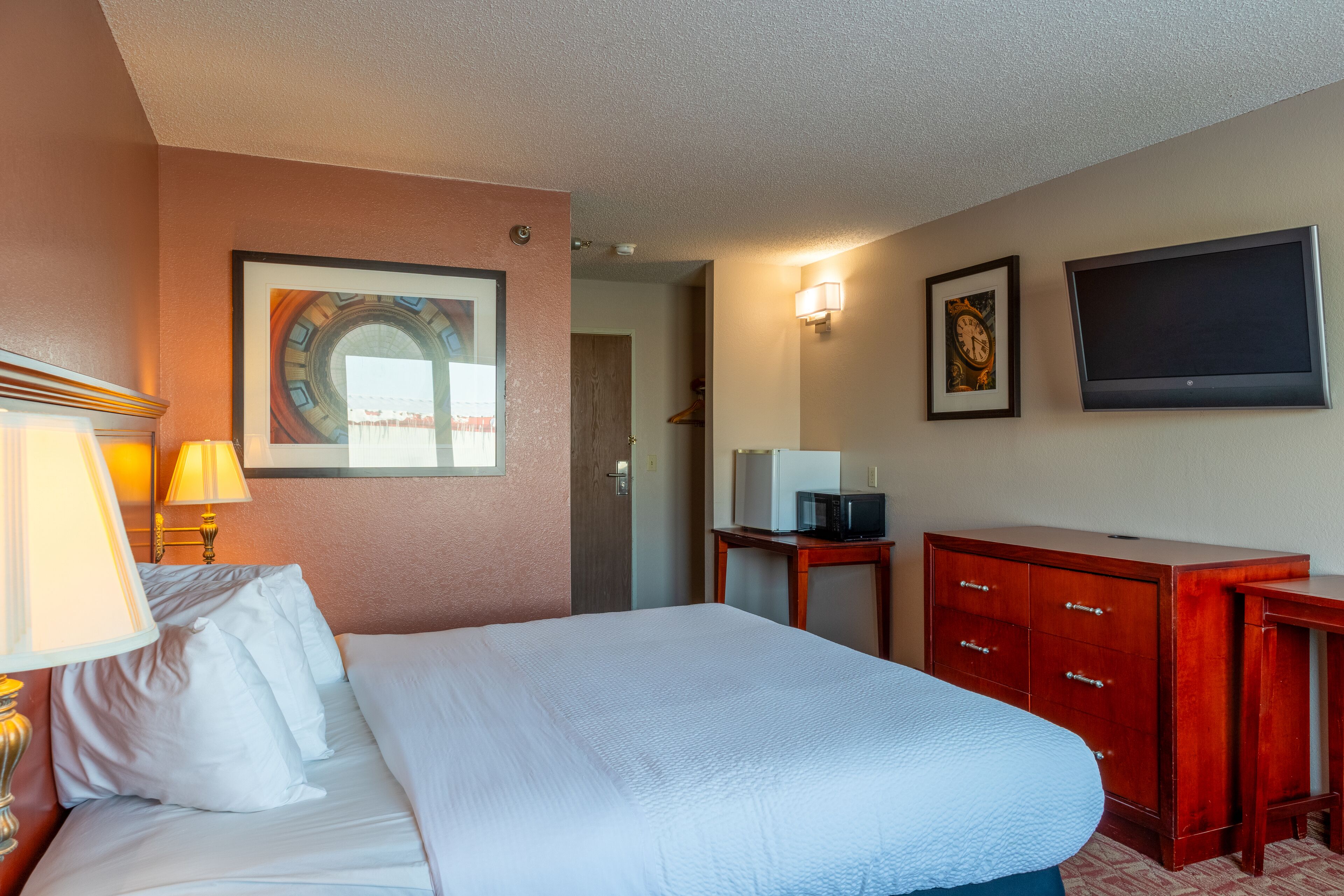A hotel room with a large bed, a wooden dresser, a television, and a framed picture on the wall.