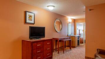 A hotel room with a wooden dresser, a flat-screen TV, a mirror, and a kitchenette.