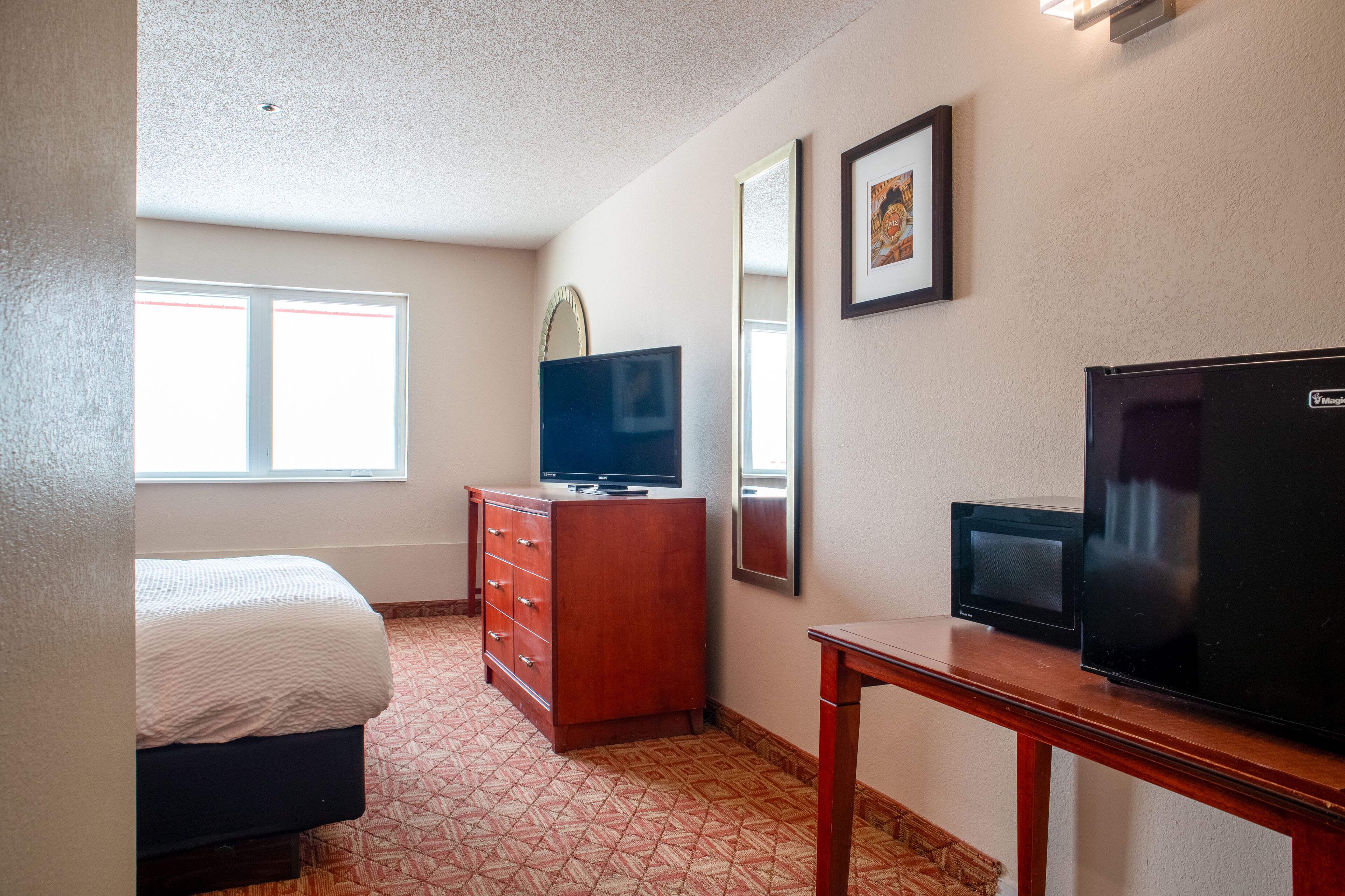 A hotel room with a bed, a dresser, a television, a microwave, and a mirror.