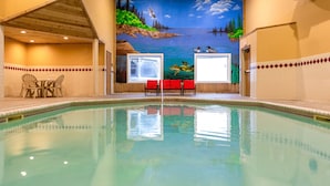 An indoor swimming pool with a mural of a lake scene, a table with chairs, and a red bench. - Norland Inn and Suites Roseau (Roseau)