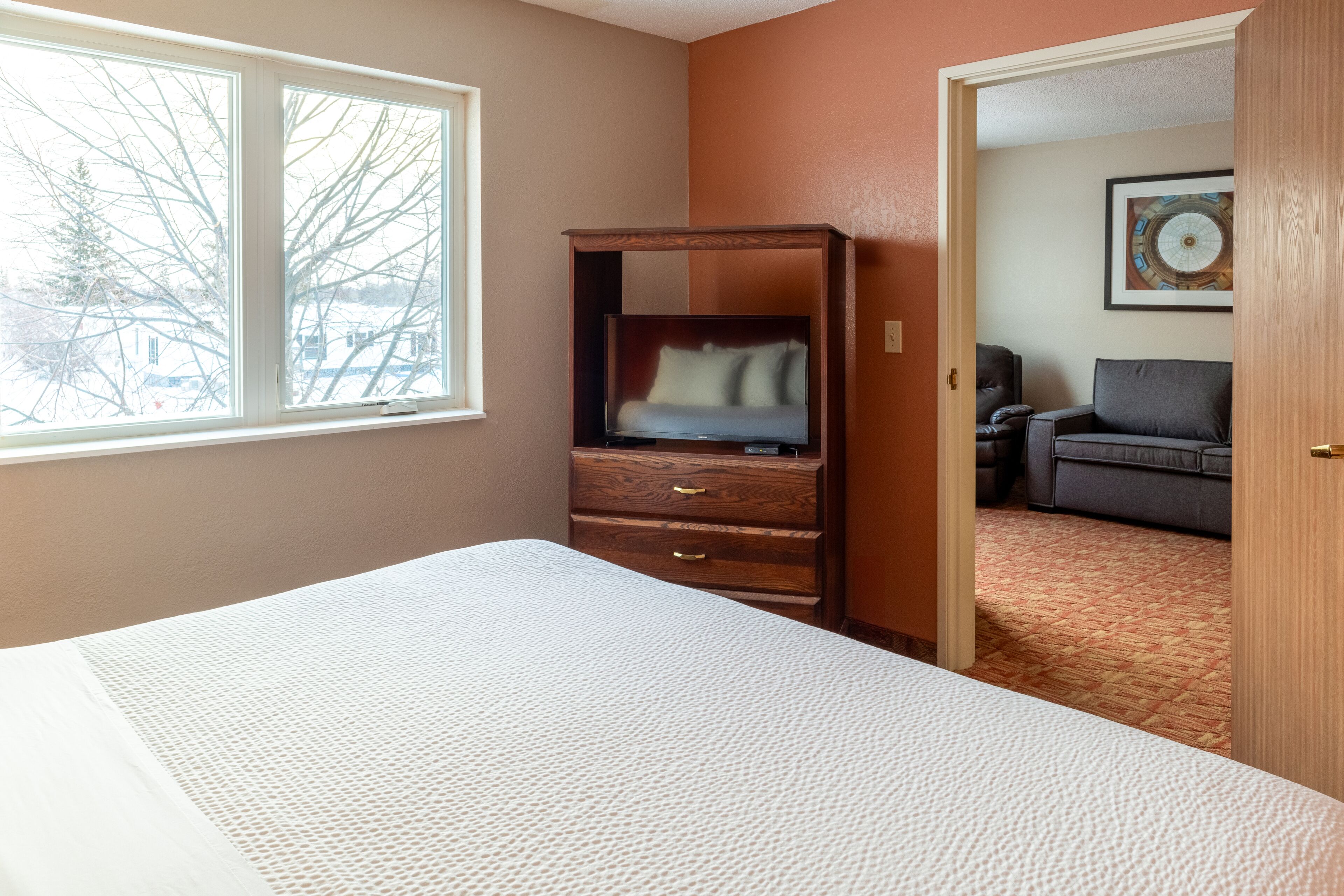 A bedroom with a bed, a dresser, a window, and a door leading to another room.