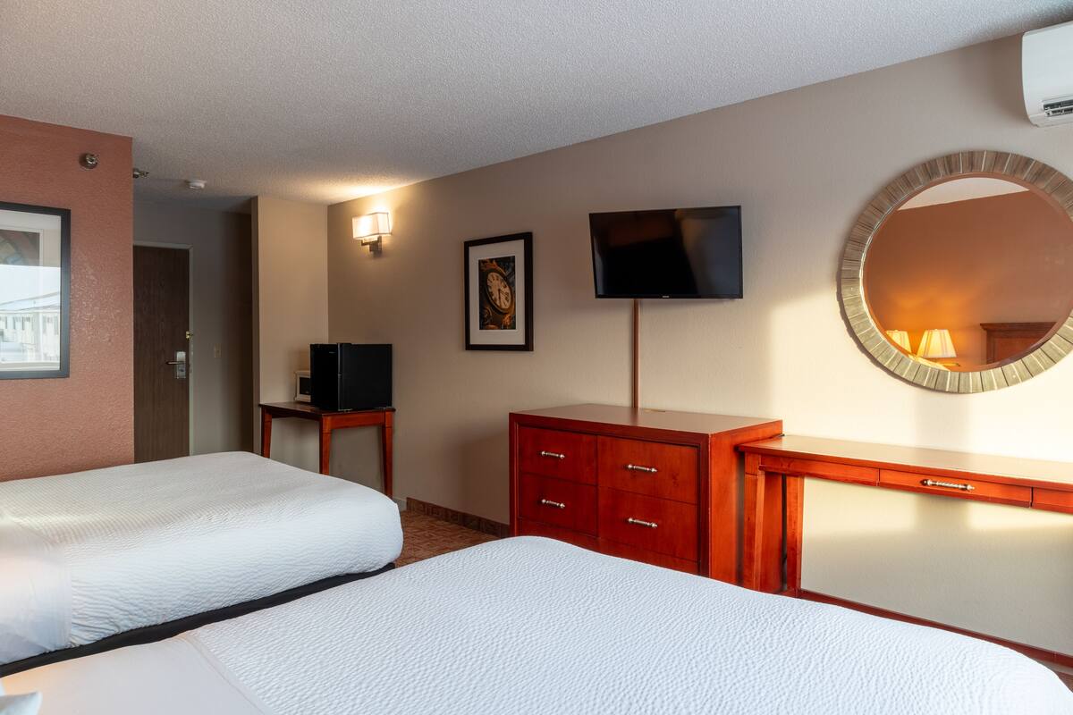 A hotel room with two beds, a TV, a mirror, and a dresser.