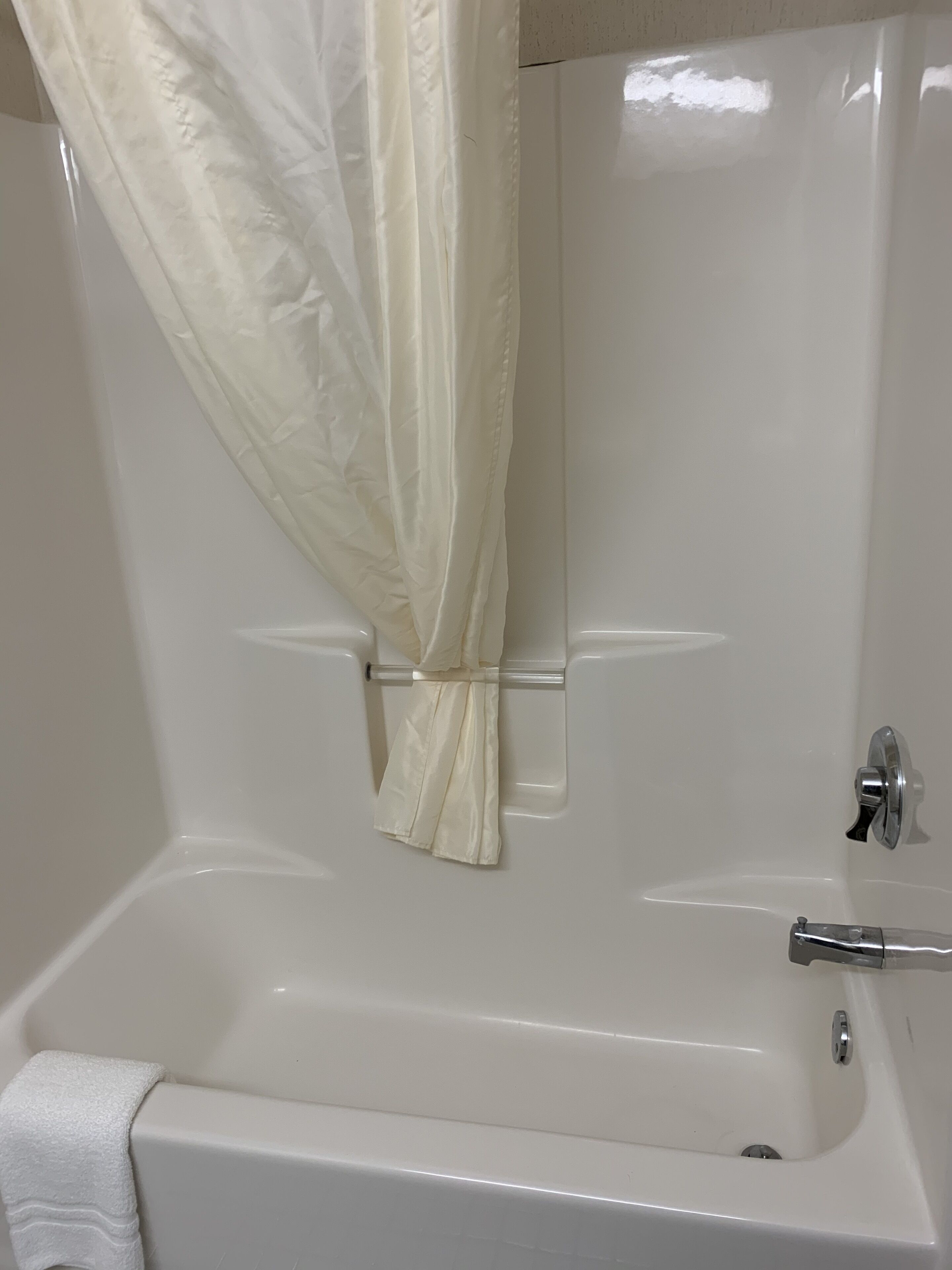 A white bathtub with a shower curtain, a towel, and a faucet.