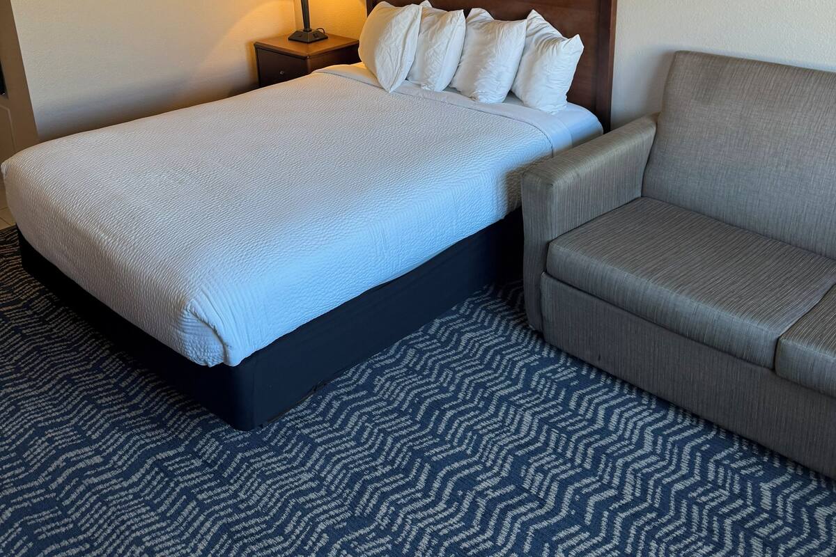 A hotel room with a bed, a nightstand with a lamp, a sofa, and two framed pictures on the wall.