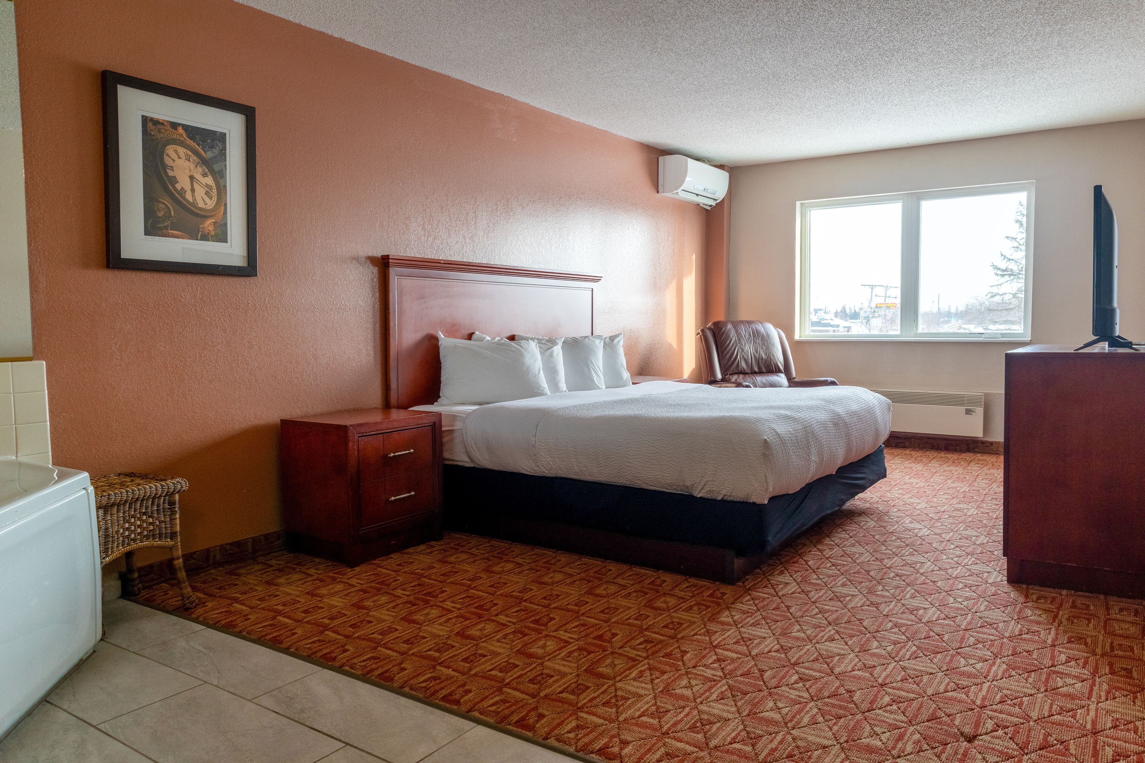 Habitación de hotel con cama, mesita de noche, cómoda, silla de mimbre y ventana con vistas al exterior.