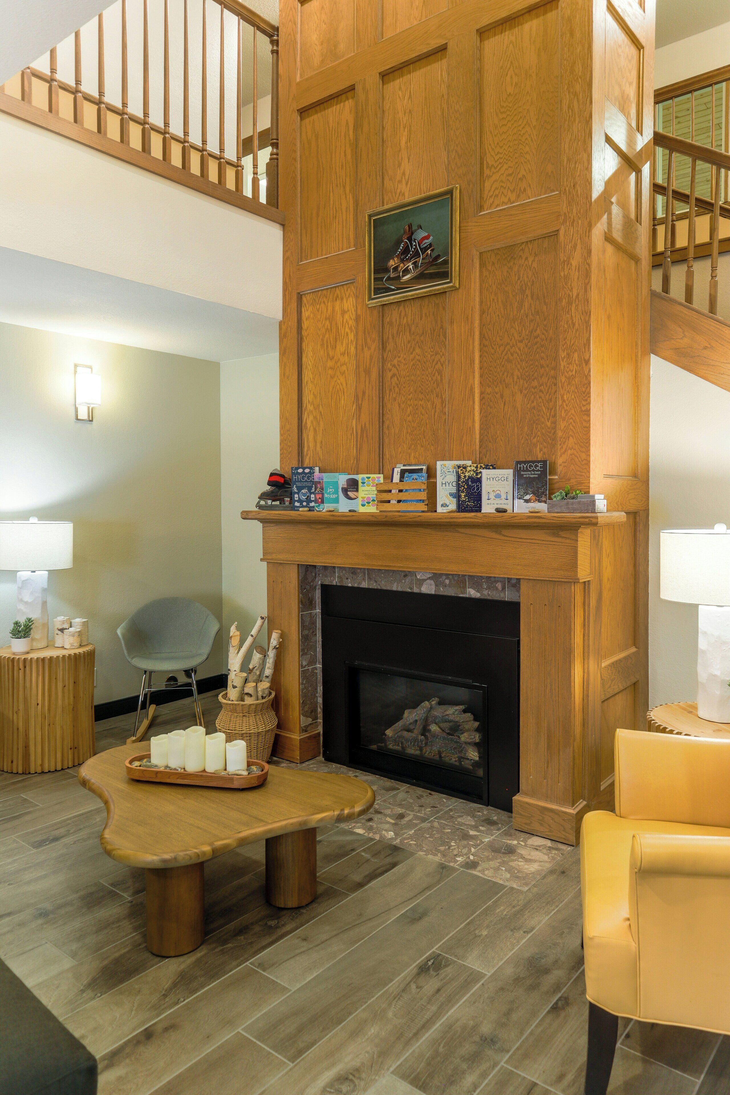 A living room with a fireplace, wooden paneling, a staircase, and a dining area.