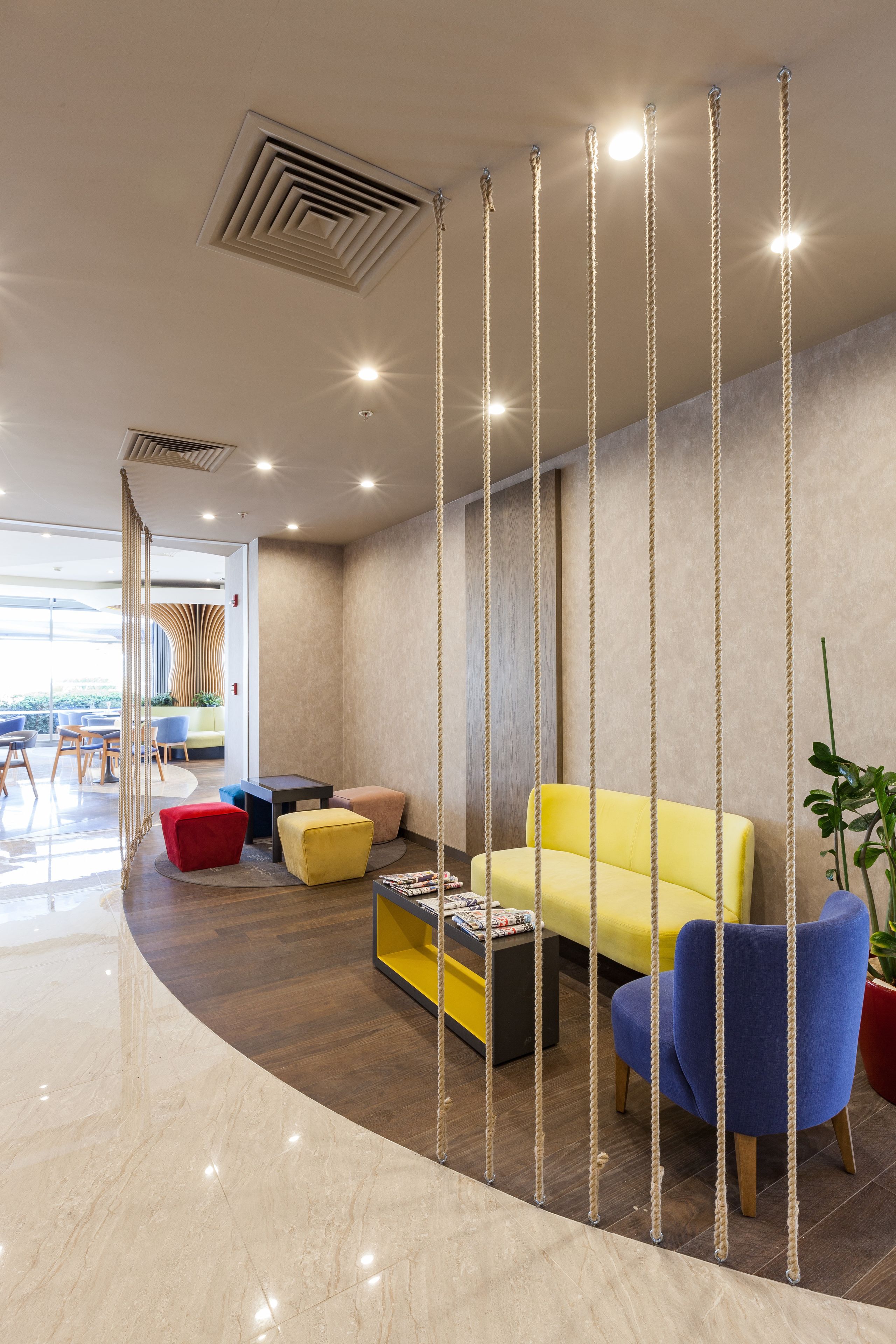 Een modern interieur met een gele bank, blauwe fauteuils en een rode poef.