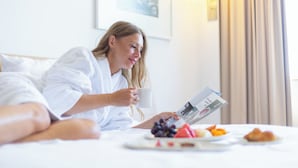 A person lying in bed with a magazine, a cup, and a plate of fruit. - Novotel Istanbul Zeytinburnu (Istanbul)