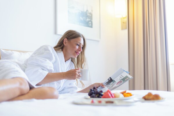 A person lying in bed with a magazine, a cup, and a plate of fruit. - Novotel Istanbul Zeytinburnu (Istanbul)