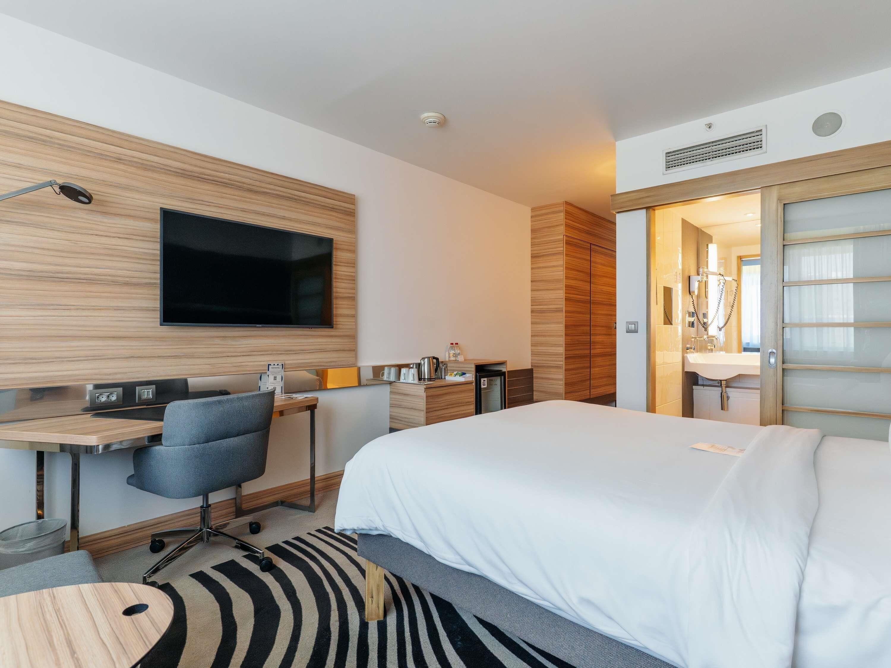 A modern hotel room with a bed, desk, chair, TV, and a bathroom with a shower and toilet.