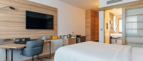 A modern hotel room with a bed, desk, chair, TV, and a bathroom with a shower and toilet.