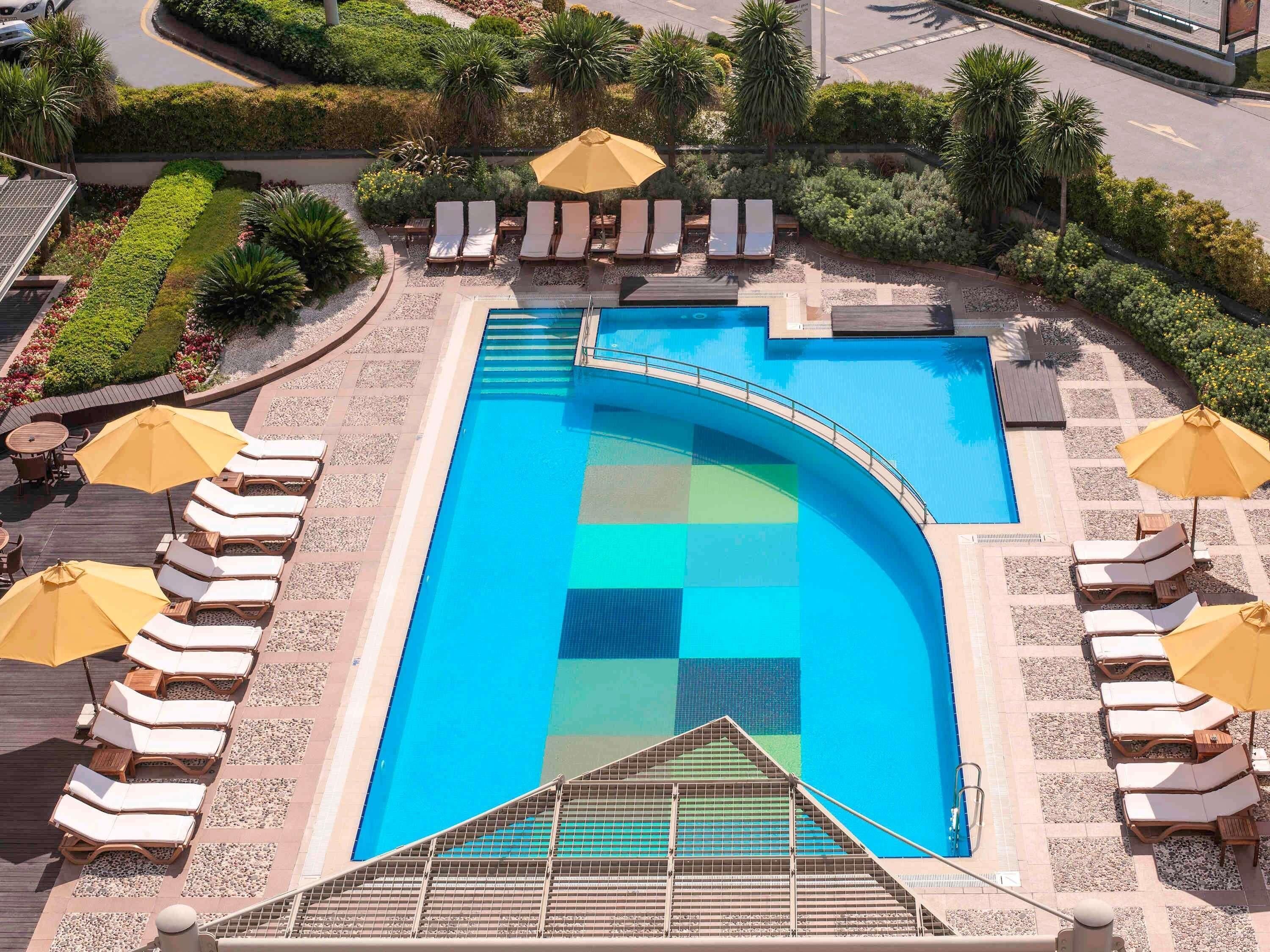 Piscina con tumbonas y sombrillas, rodeada de jardines ajardinados.
