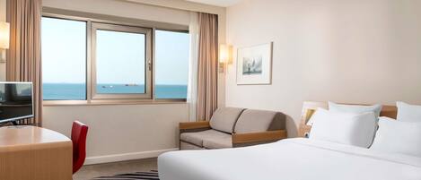 Habitación de hotel con cama, escritorio, silla, televisión y ventana con vista al mar.
