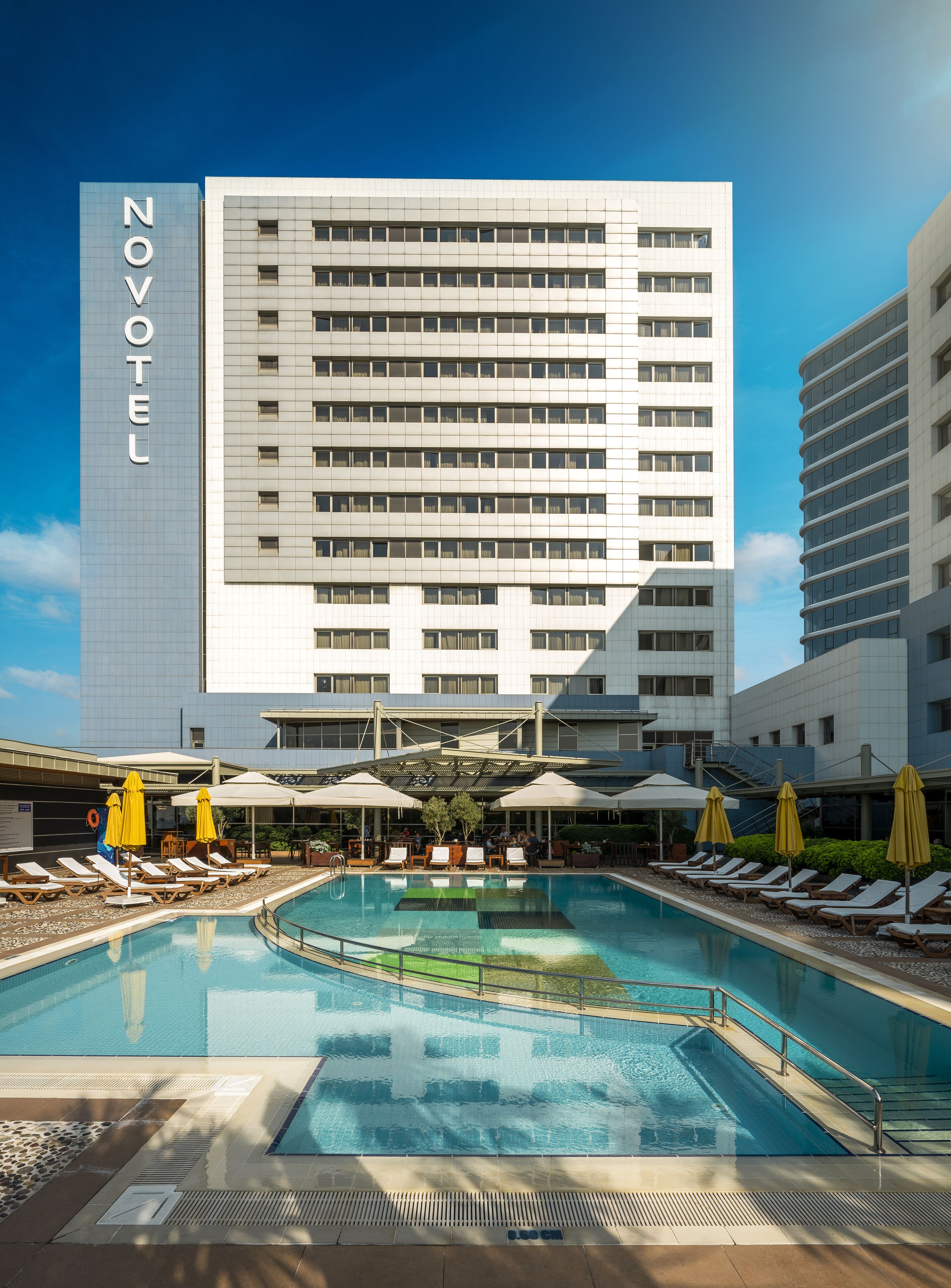 A Novotel hotel with a swimming pool, sun loungers, and umbrellas.