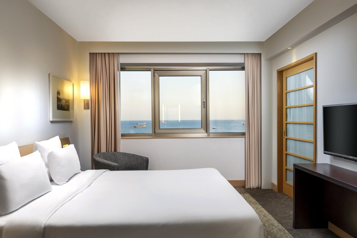 Habitación de hotel con una cama grande, una silla, un televisor y vistas al mar.