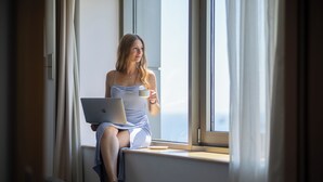 A person sitting by a window with a laptop and a cup, in a room with curtains and a view. - Novotel Istanbul Zeytinburnu (Istanbul)