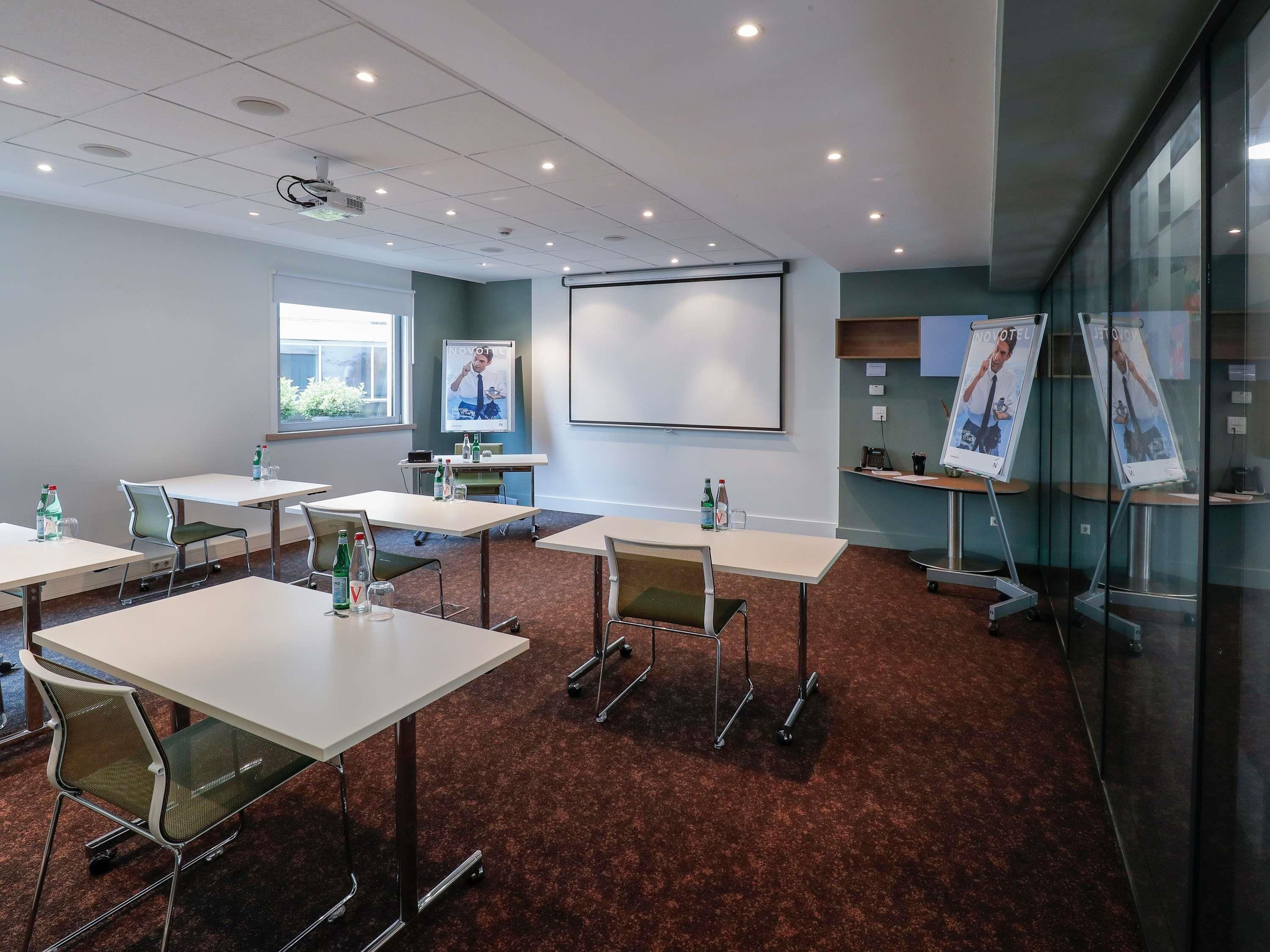 A conference room with tables, chairs, a projector, a whiteboard, and glass walls.