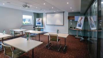 A conference room with tables, chairs, a projector, a whiteboard, and glass walls.