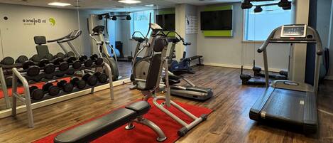 Un gimnasio con cintas de correr, elípticas y una banca.
