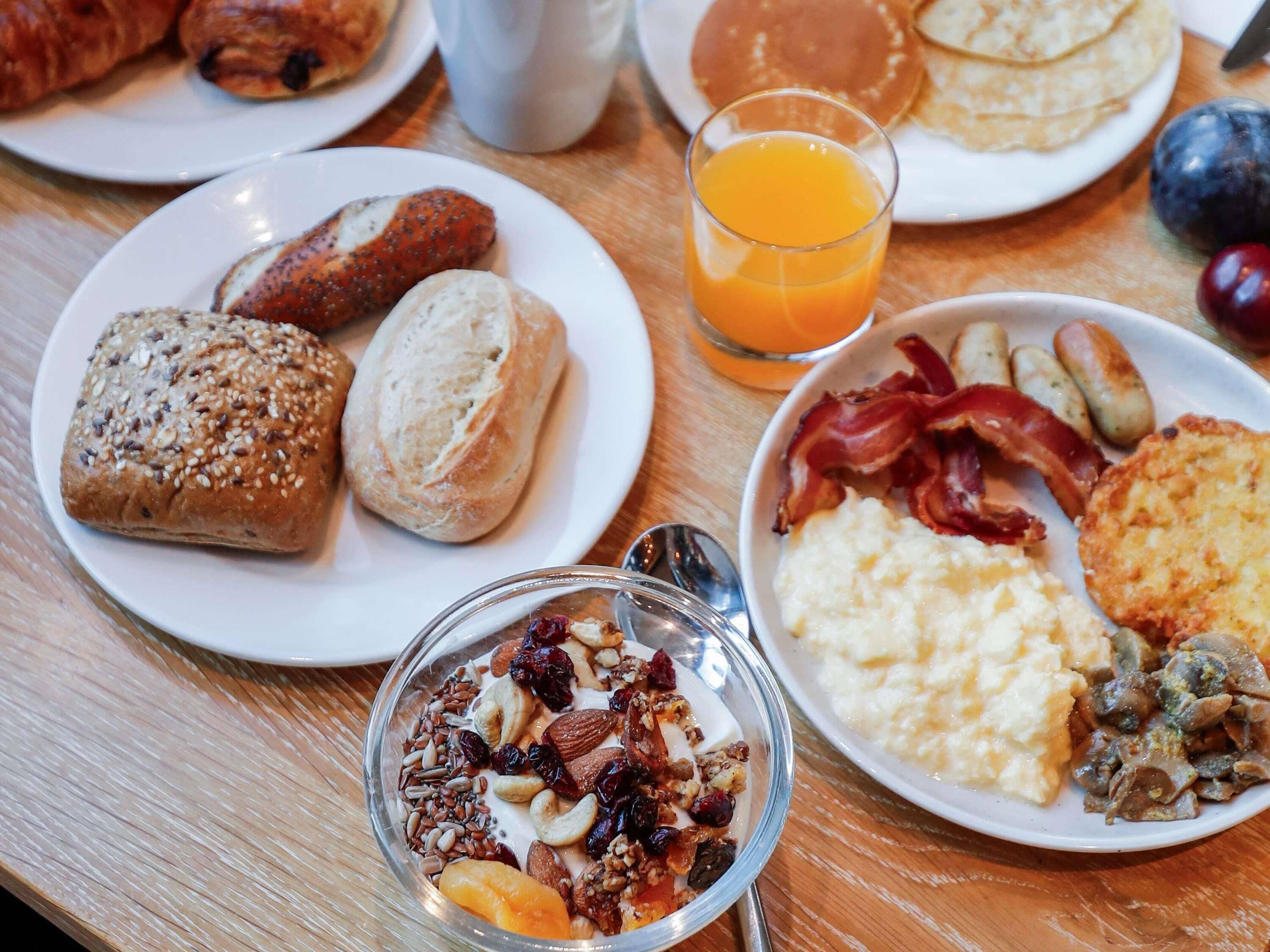 A breakfast table with various food items including bread, eggs, bacon, and a bowl of cereal.