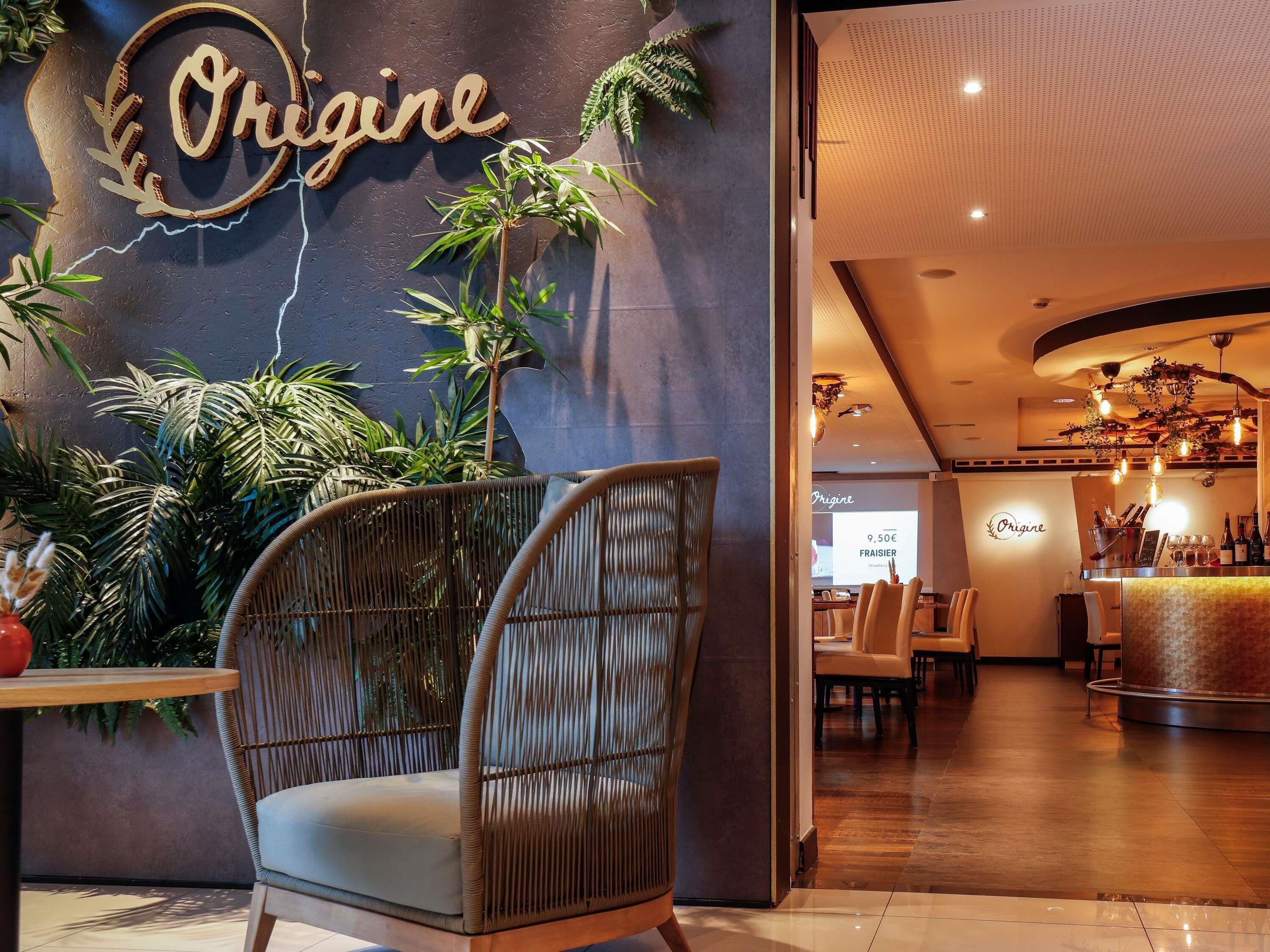 Een modern interieur met een rieten stoel, een bar en een bord waarop 'Origine' staat.