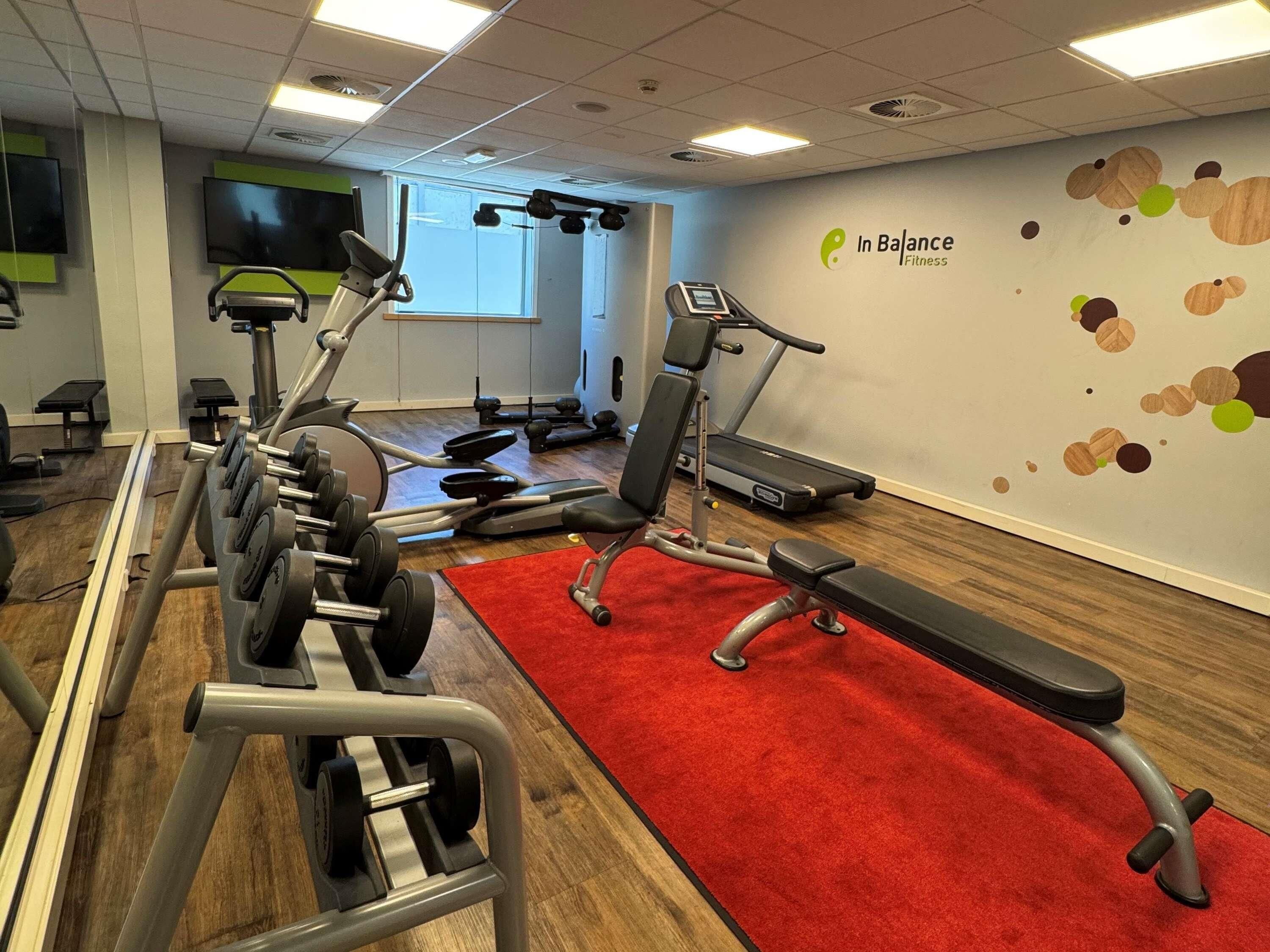 Een fitnessruimte met trainingsapparatuur, een rode loper en een muur met een logo.