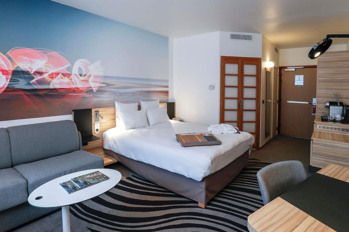A modern hotel room with a bed, a sofa, a small table, and a desk.