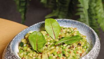 A bowl of lentil salad with green leaves on a wooden table.