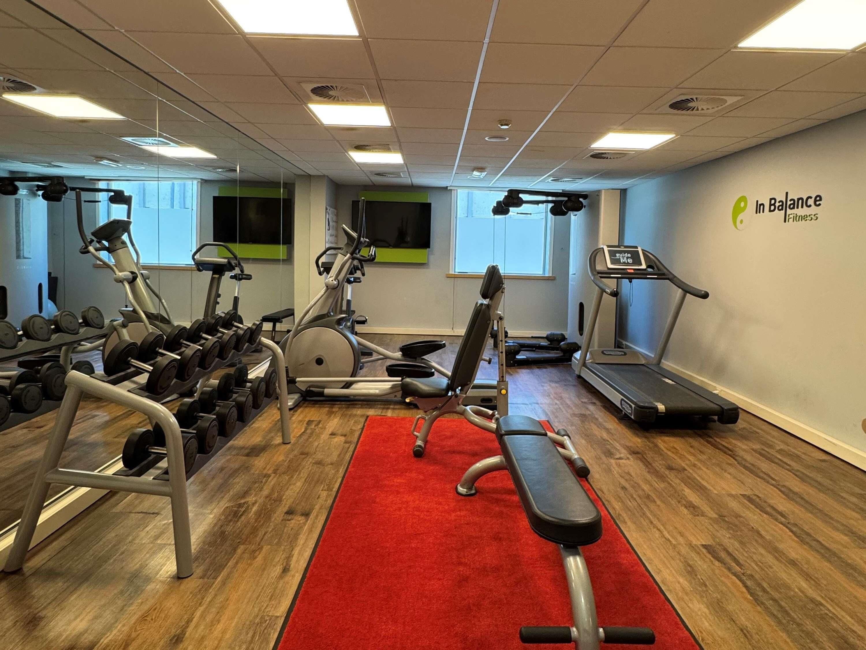 Een sportschool met trainingsapparatuur, een rode loper en een bord waarop 'In Balance Fitness' staat.