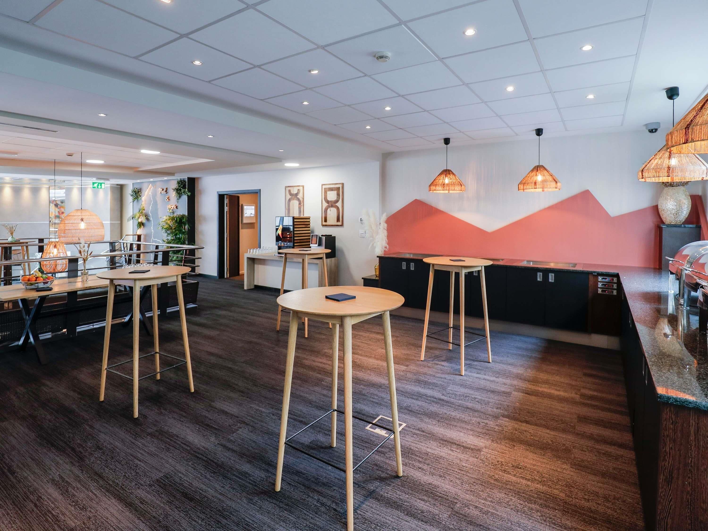 A modern hotel lobby with wooden tables, a reception desk, and a wall with abstract art.